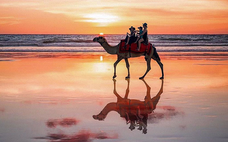 Three people riding on a camel on the beach in Broome